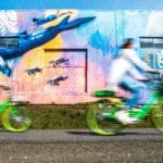 People riding bikes on the Burke Gilman next to a mural.