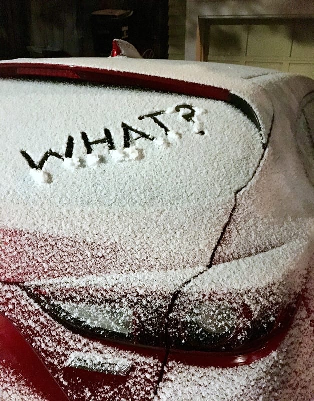 Car covered in snow with the word "what?" inscribed on the back of the car