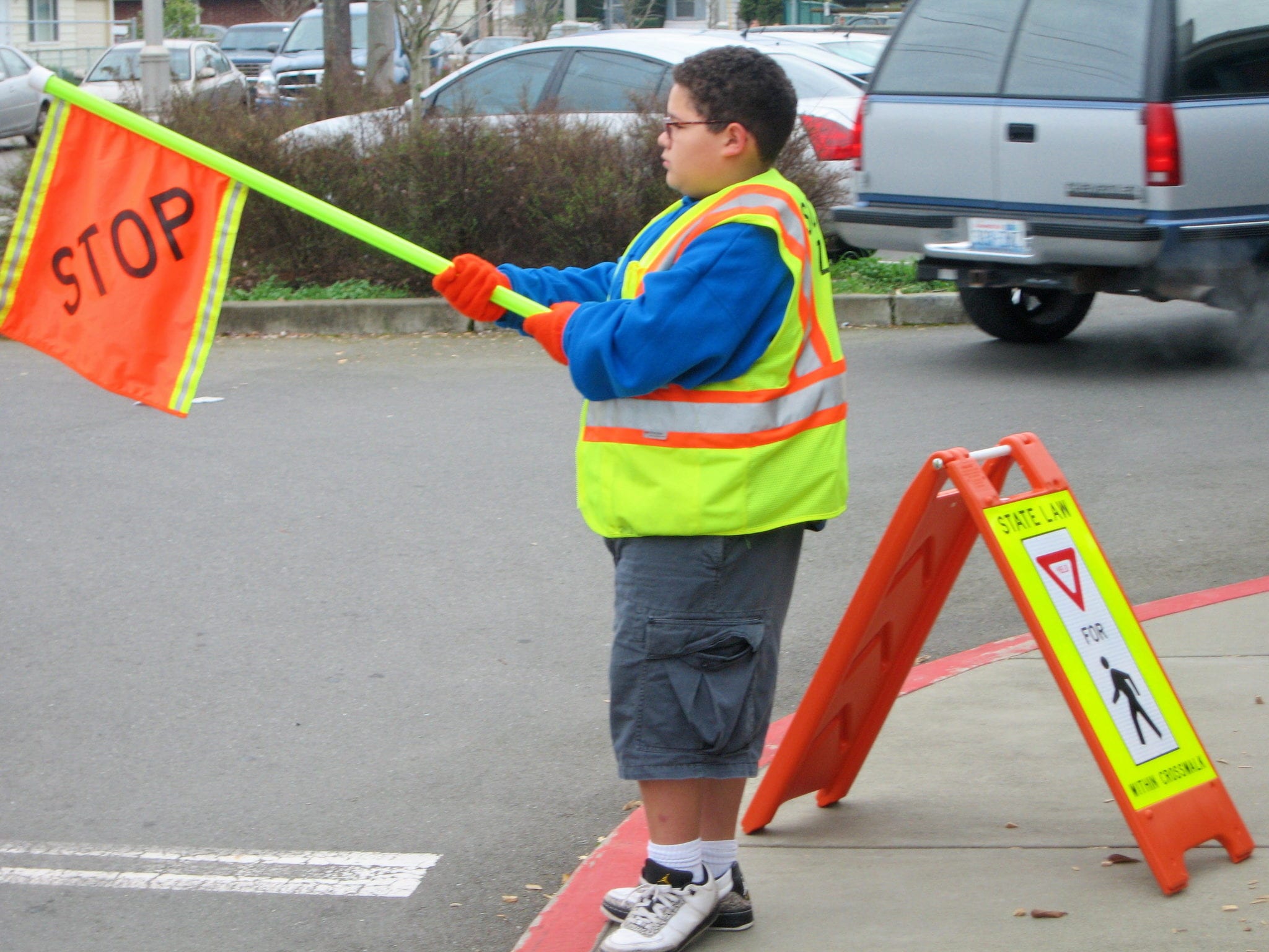 A person holding a stop flag in a school parking lot.