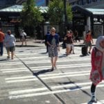 People walking across a crosswalk near a light rail station.