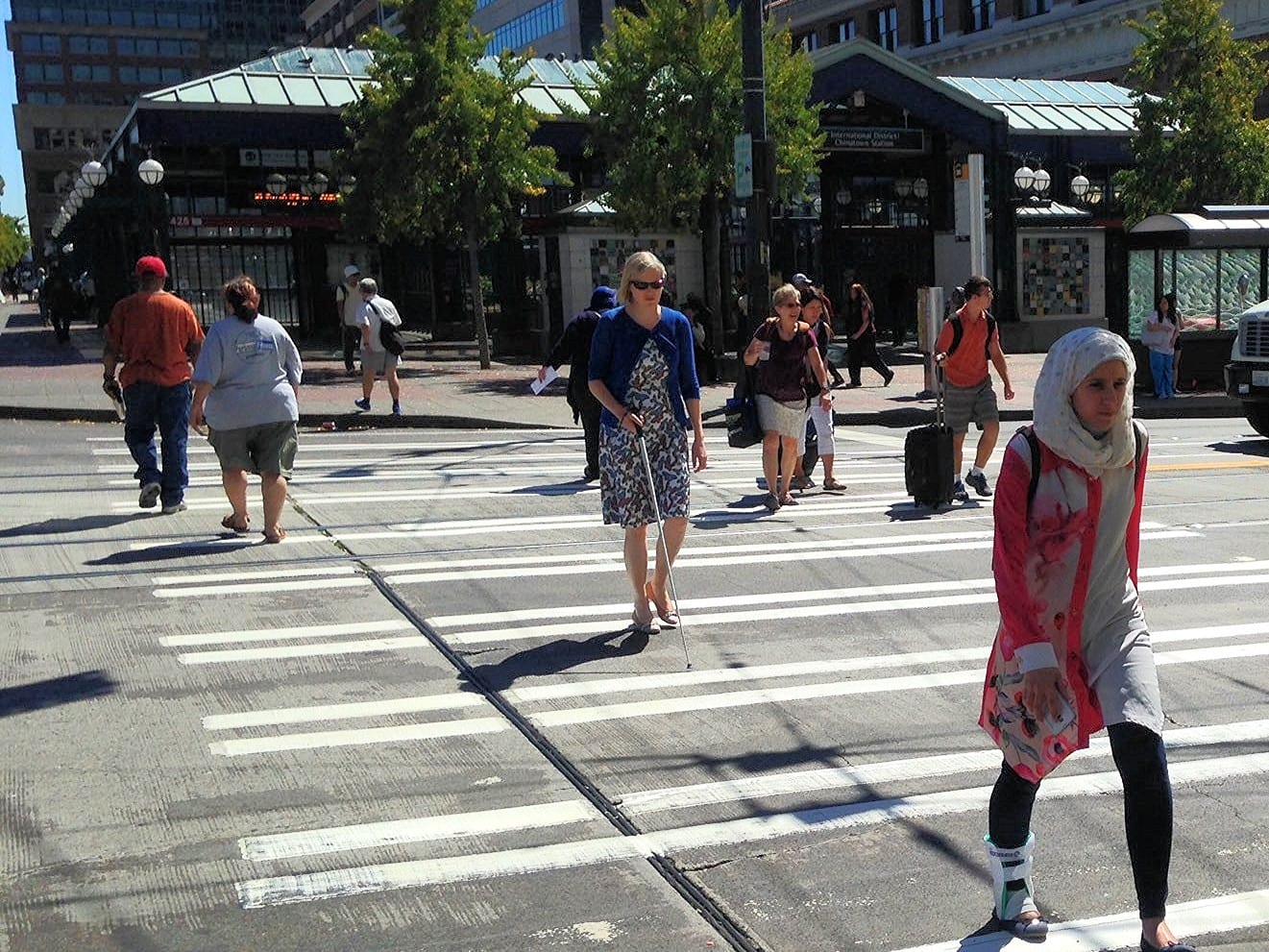 People walking across a crosswalk near a light rail station.