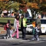 Children and their parents walking across a crosswalk on their way to school.
