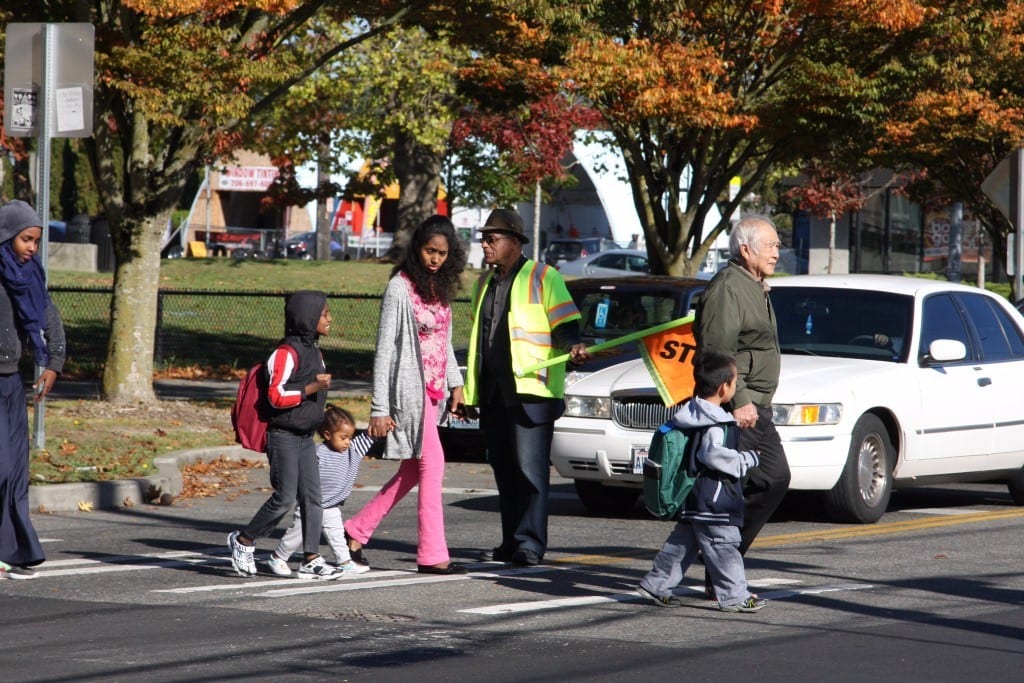 Children and their parents walking across a crosswalk on their way to school.