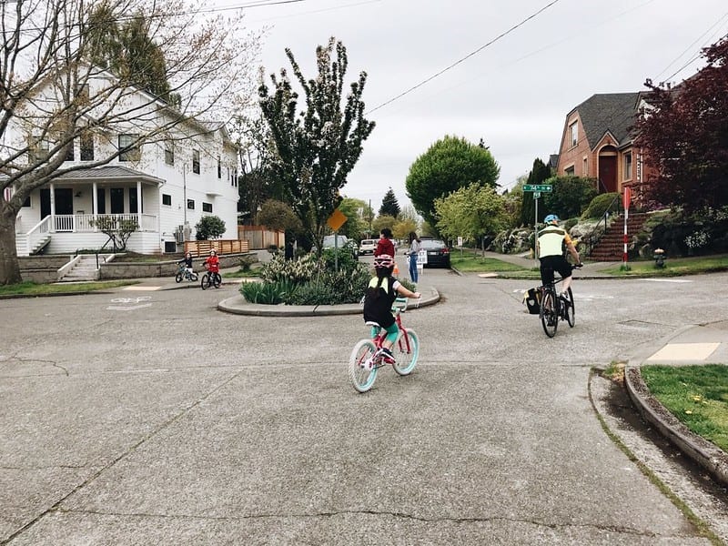 Adults and children bike riding around a roundabout on a Stay Healthy Street in Seattle.