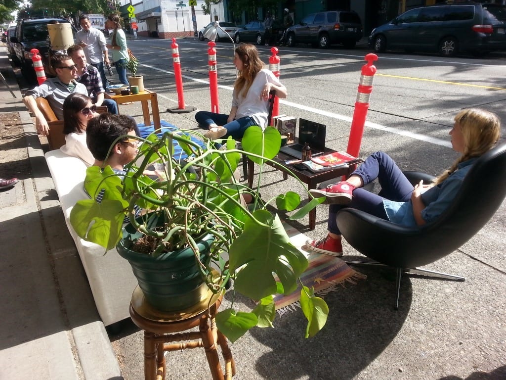 Community members sitting in a parking spot, reimagined as an outdoor patio, in 2013 on PARK(ing) Day in Seattle. Photo Credit: SDOT Flickr. 