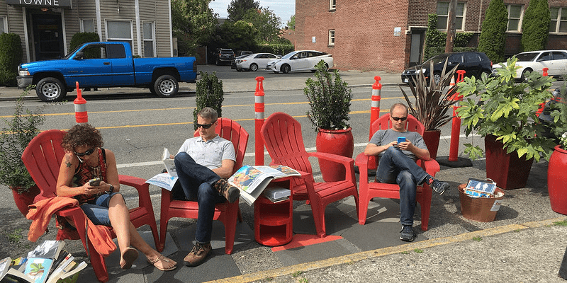 Seattle residents relaxing in red chairs in a parking space usually reserved for cars. Photo Credit: SDOT Flickr