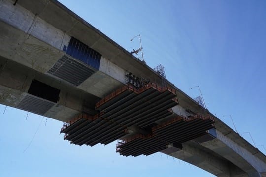 View from below: the two work platforms are suspended under the bridge, surrounded by the CFRP crews recently installed.