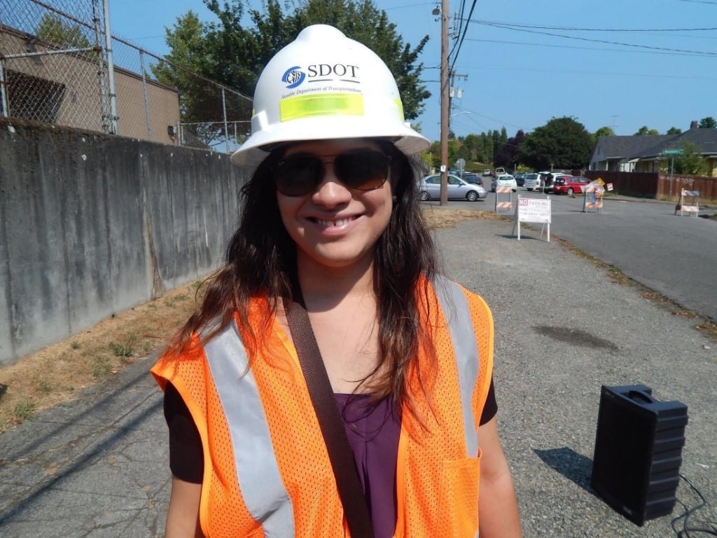 SDOT's Sonia Palma in a hard hat and orange vest standing on the sidewalk.