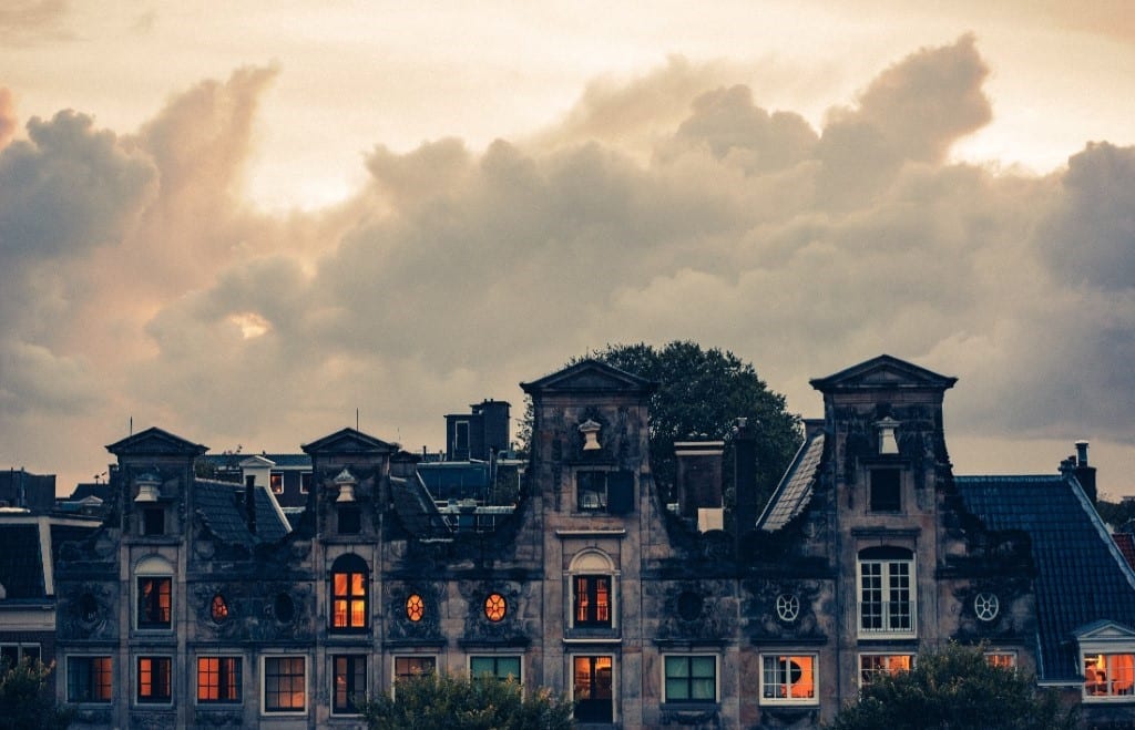Somewhat cartoonish-looking row of homes against a cloudly backdrop. Image is intentionally spooky. In windows, orange light can be seen.
