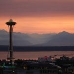 Seattle Space Needle and mountains in the distance shown at sunset.