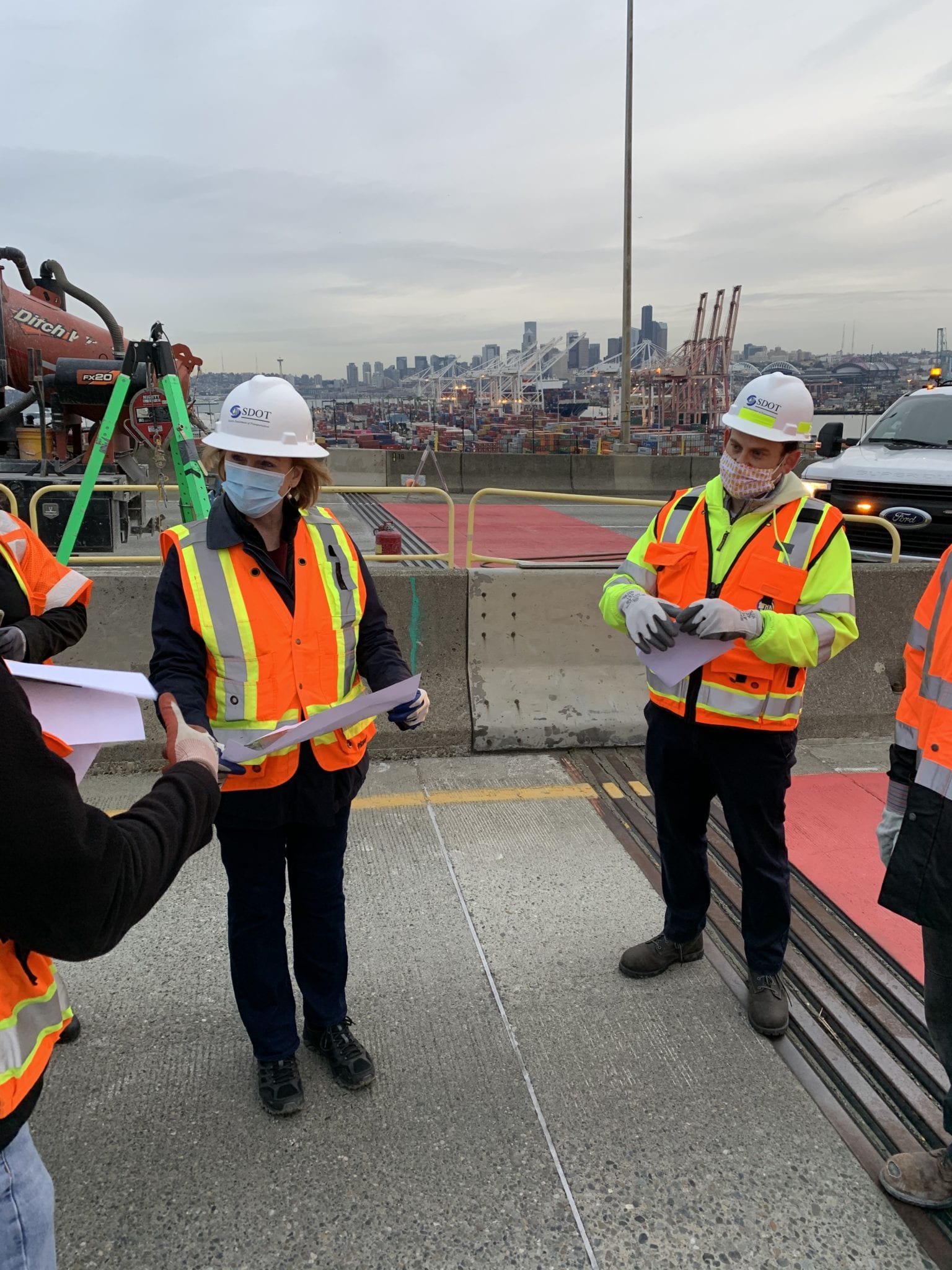 Mayor Durkan visits the West Seattle High-Rise Bridge stabilization site with SDOT Director Sam Zimbabwe and a bridge engineer. The three are looking at paper, standing on the road on the West Seattle Bridge.