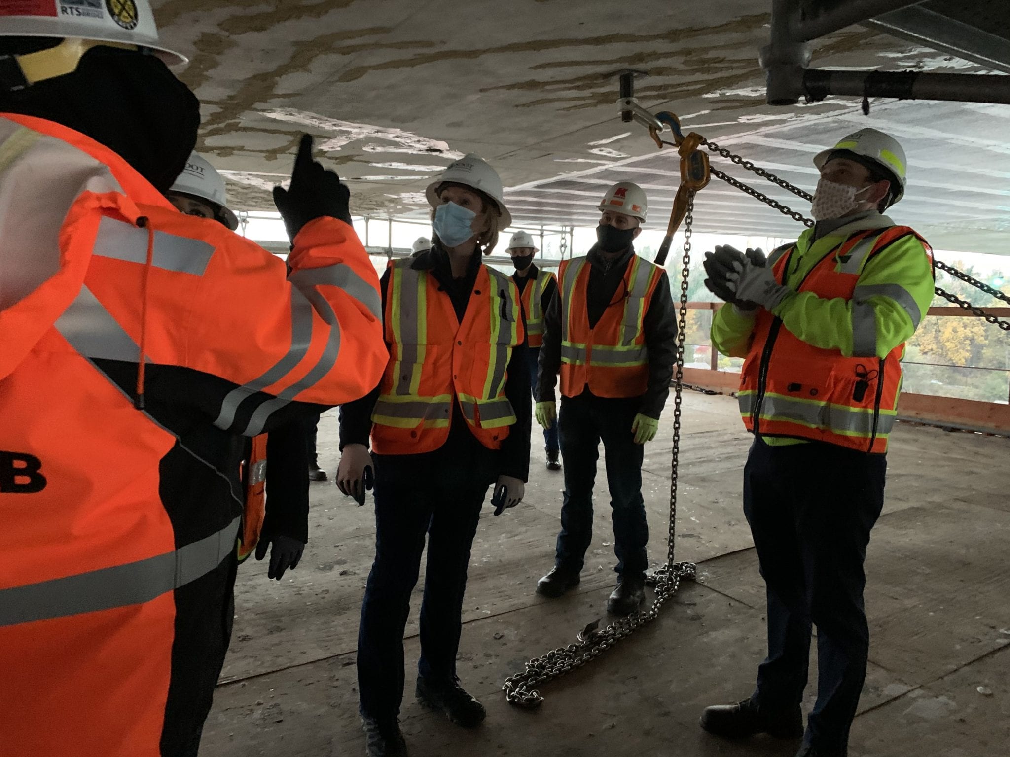 Mayor Durkan and other visitors stand on the West Seattle Bridge work platforms and point up at the bridge.