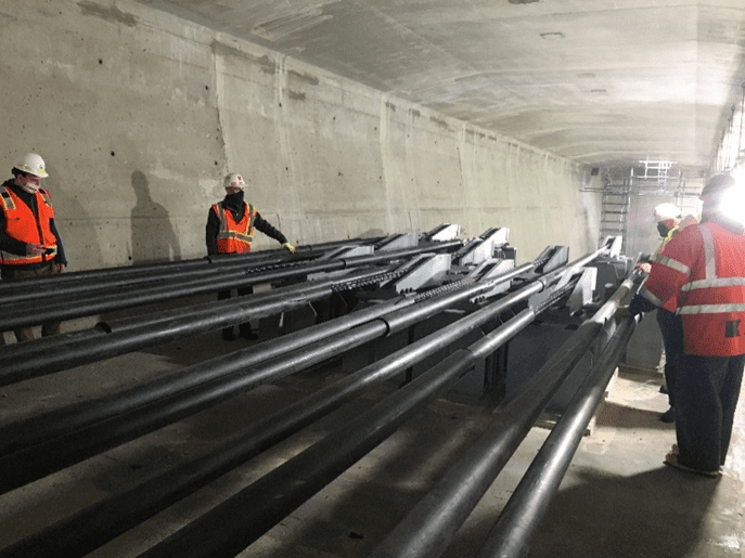 Crews standing in West Seattle Bridge girder, looking at and touching the post tensioning strands which are black, long, cylinders running parallel to the bridge inside the girder.