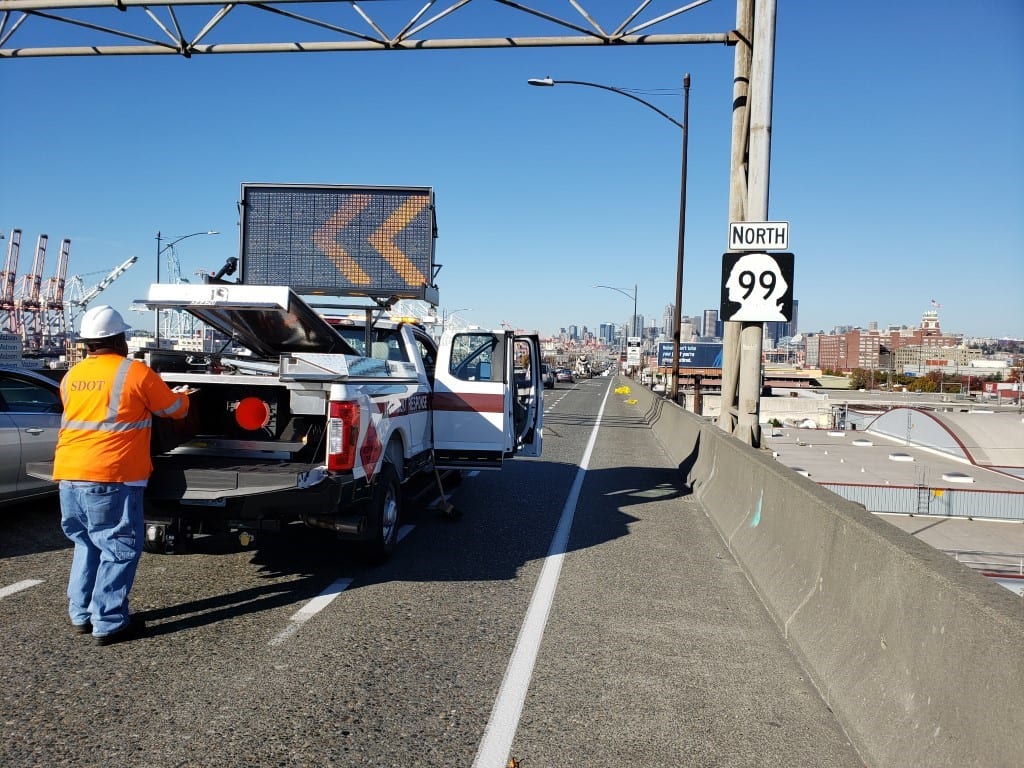 Person standing behind white SDOT response team truck on SR 99, with a digital sign showing arrows facing left.