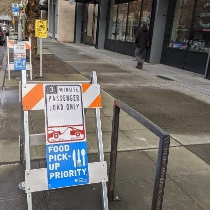 Barrier with sign reading "3 minute parking only" and a blue "Food Pick Up Priority" sign.