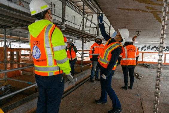 Mayor Jenny Durkan and SDOT Director Sam Zimbabwe on the West Seattle Bridge work platform looking and pointing at the underside of the bridge.