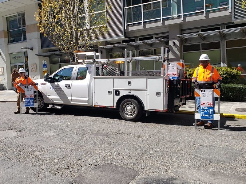 Two SDOT crew carrying food priority pick up signs from a white SDOT pickup truck.