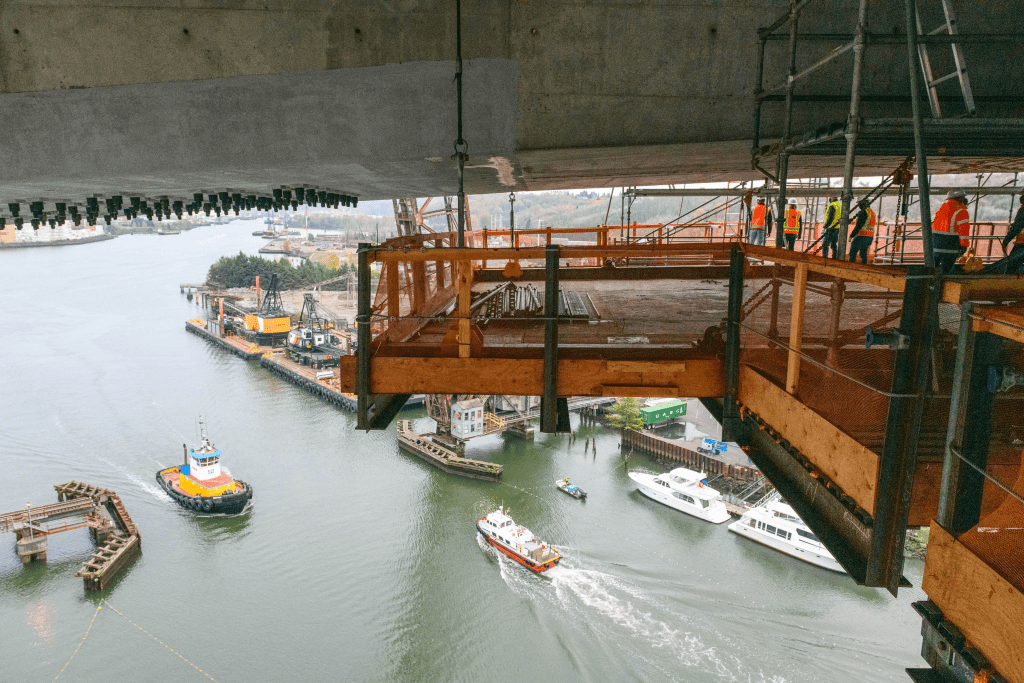 The photo is taken by someone standing on the West Seattle High Rise Bridge work platforms which are suspended under the bridge. The Duwamish waterway with boats crossing under the bridge can be seen below.
