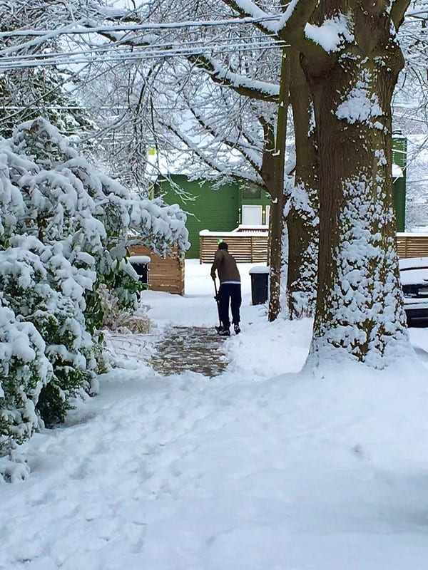A person shoveling snow on a sidewalk on a very snowy day in Seattle.