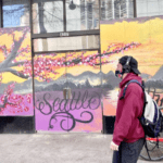 Person walking past a colorful mural that says "Seattle" on the side of a building.