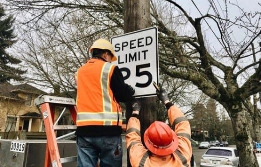 Crew hanging a 25 mph speed limit sign on a wooden post.