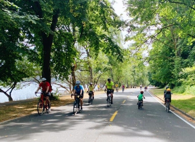 A group of people bike riding on a sunny day along Lake Washington Boulevard.