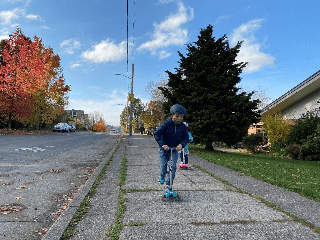 Children riding stand up scooters on a sidewalk.