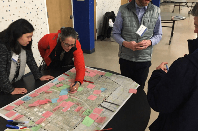 Four people near a map on a table at a community outreach and engagement event. Two people are looking at and marking the map.