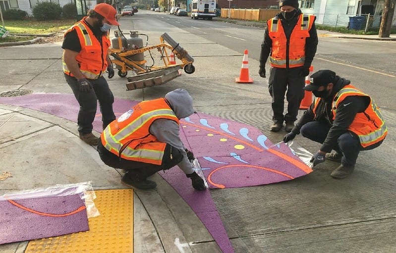 Crews installing purple artistic curb bulbs on 8th Ave S.