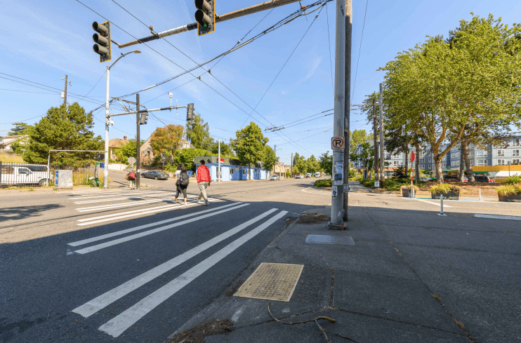 Street-level view of a crosswalk at Rainier Ave S and S Rose St, with two people crossing it.