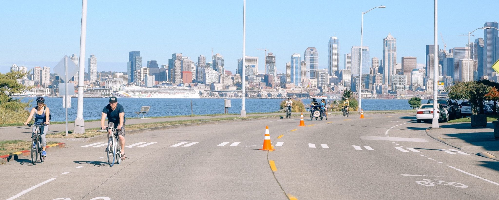 People riding bikes along Alki Beach with Seattle Skyline in background