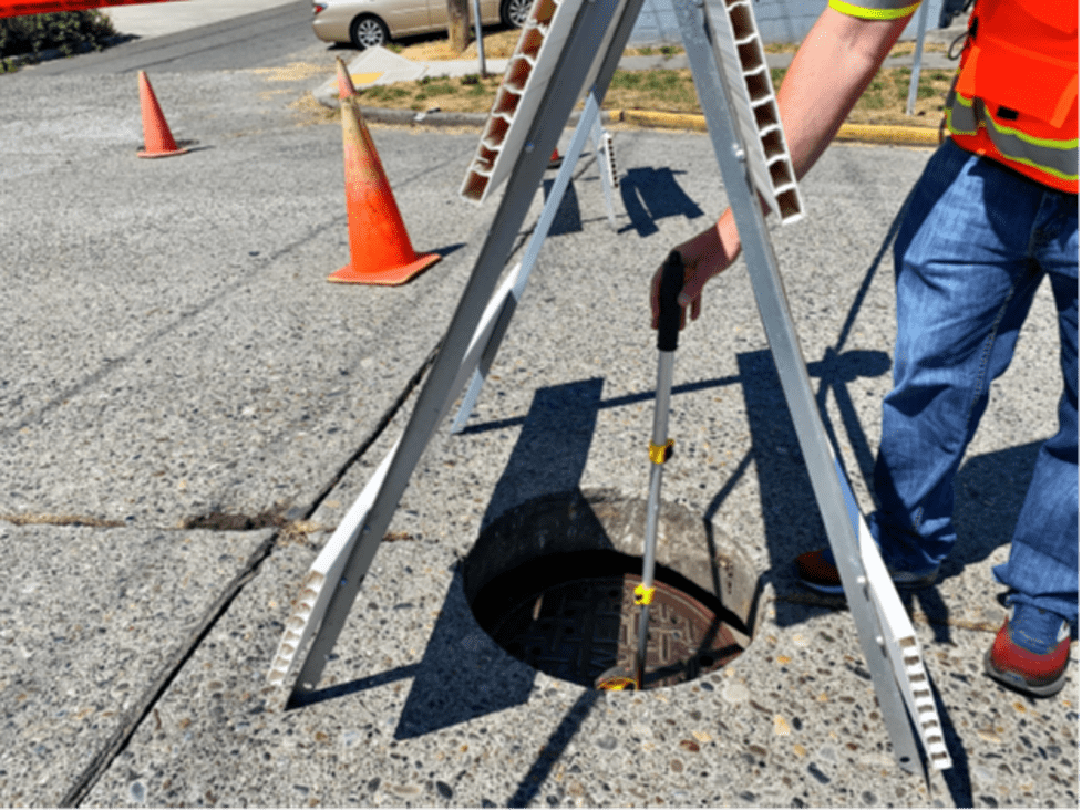 Workers measuring how high the swollen pavement has risen above a utility maintenance hole.  