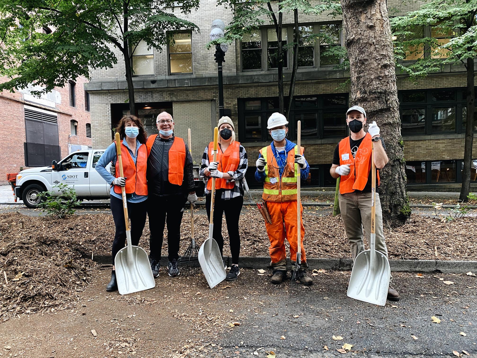 A group of five volunteers holding three shovels work to install new landscaping in Seattle's Pioneer Square neighborhood.