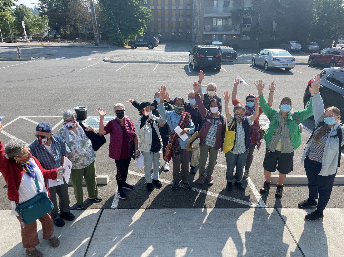 Community members who participated in a transit field trip for seniors in fall 2021. Around a dozen people can be seen smiling and waving at the camera from a parking lot.