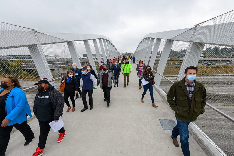 Pedestrians walk across the new John Lewis Memorial Bridge, which crosses Interstate 5 in north Seattle, in the Northgate neighborhood. Many walkers walk toward the camera with masks on, enjoying the new bridge.