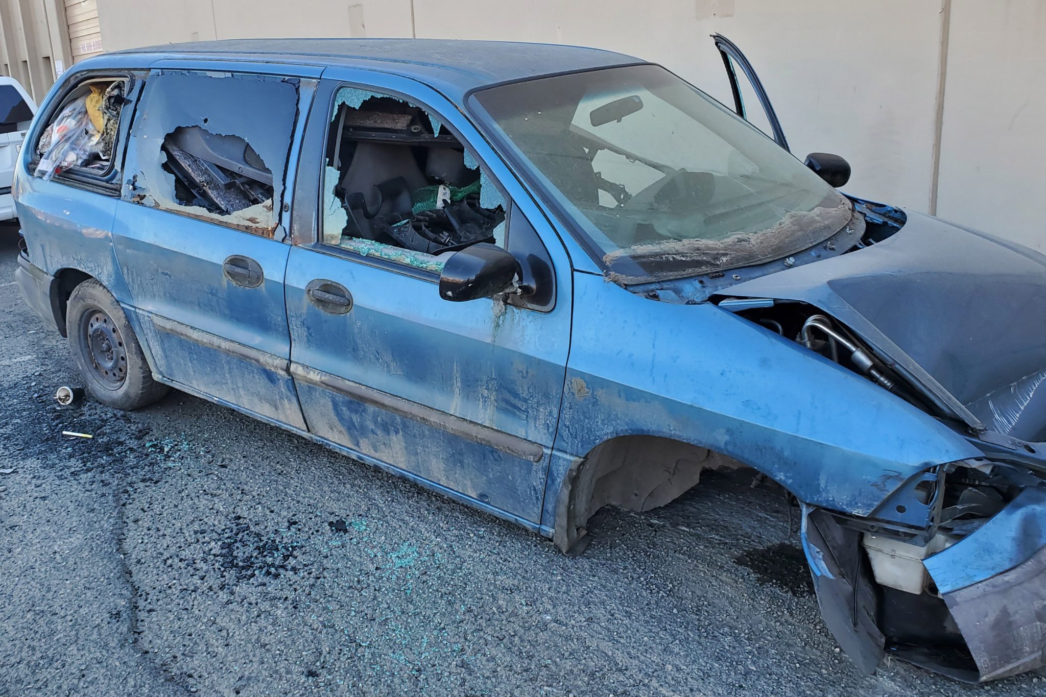 A blue abandoned vehicle pictured on a street in the City of Seattle. The vehicle's wheels are missing and the driver's side door is open.