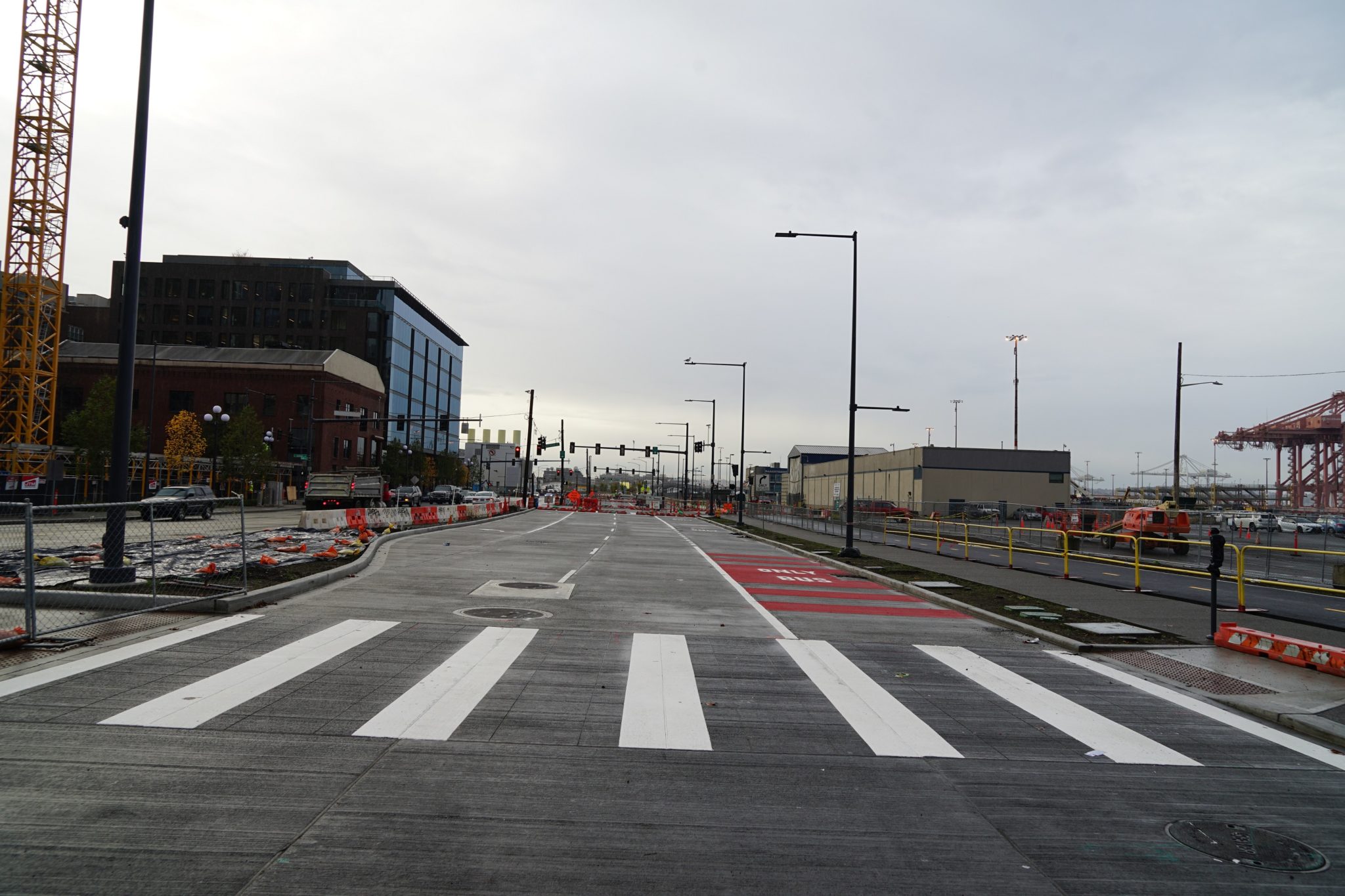 A photo of the newly paved Alaskan Way S at S Main St. The image shows the new roadway, with a marked crosswalk in the foreground. Buildings are visible in the background, along with several street lights.