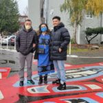 Artist Romel Belleza (on the right) stand with his parents on top of the new mural at NE 140th St and 32nd Ave NE.