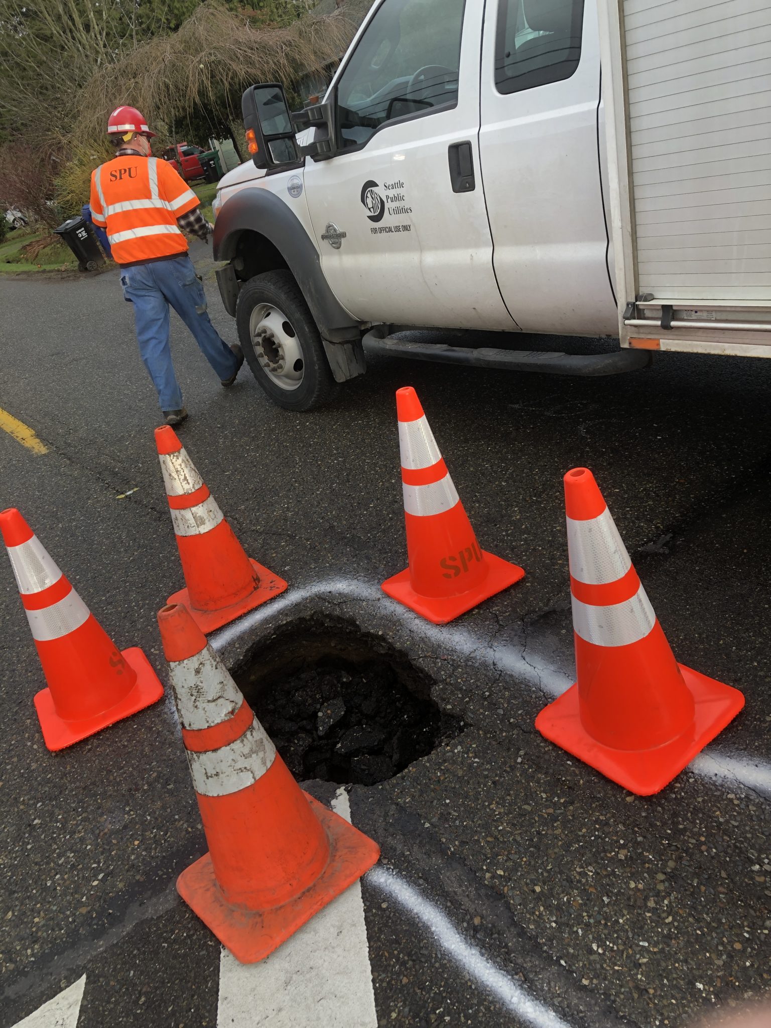 Seattle Public Utilities worker installing road safety cones around sink hole.