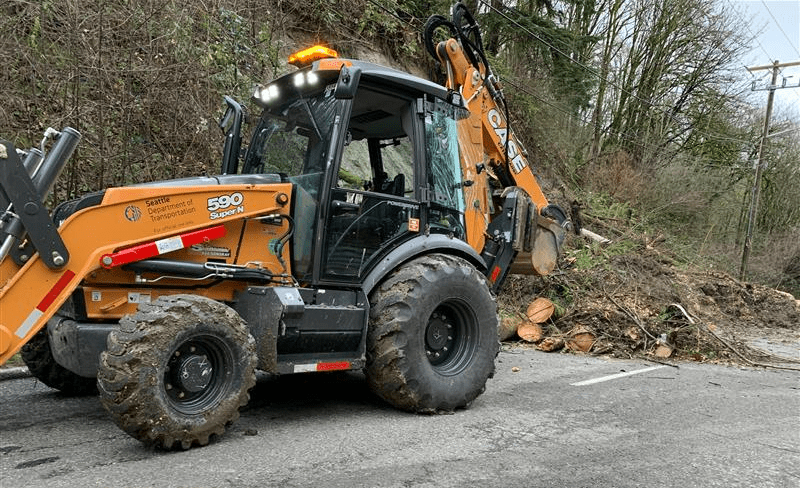 Photo of a large excavator working to clear trees and debris from a section of Highland Park Way SW in West Seattle.