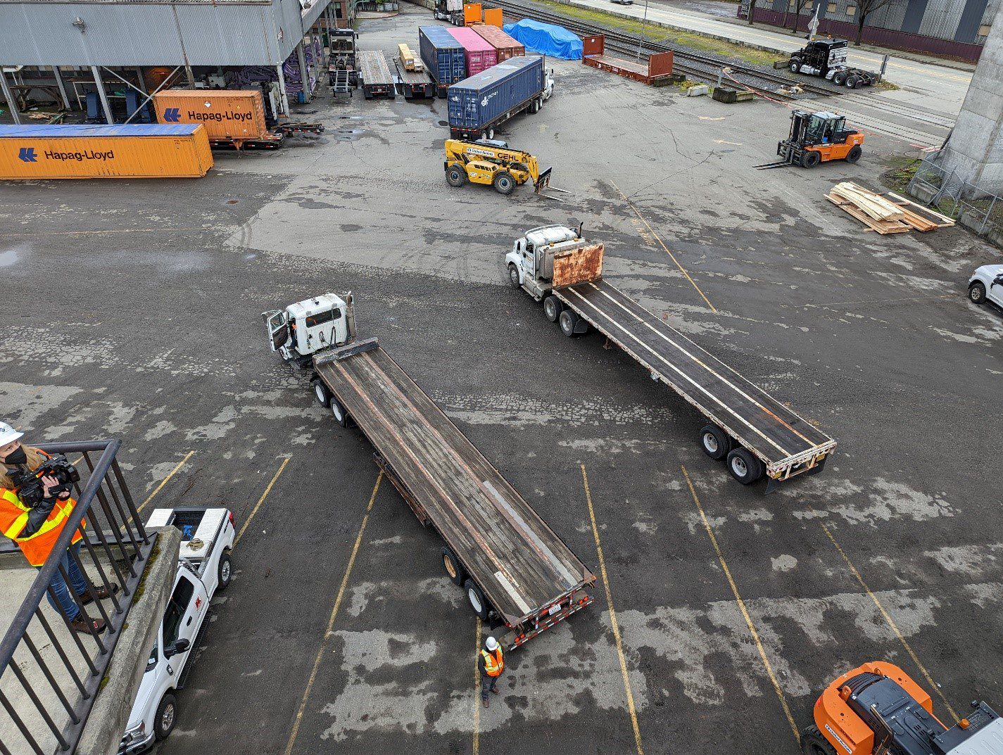Two platform bed trucks await the first of two work platforms that were hoisted into place on Saturday, January 8. The platforms were lifted by cranes and forklifts onto the truck beds, then driven into position underneath the bridge in the hoisting area.