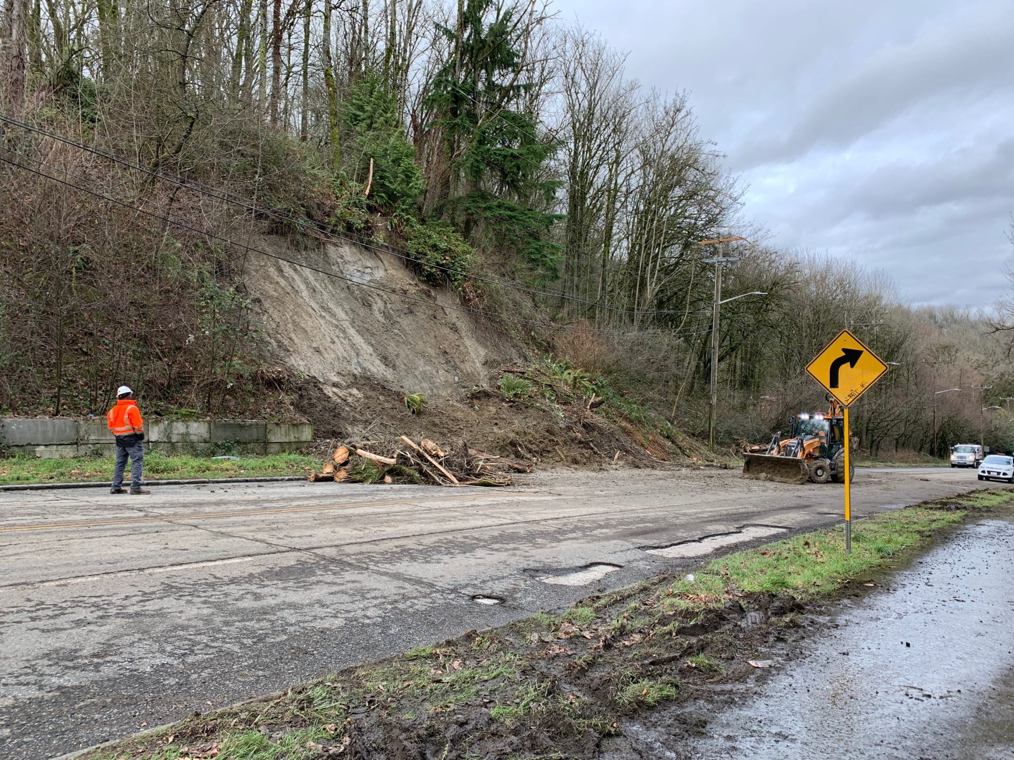 This photo shows clean-up activities along Highland Park Way SW on Saturday, January 8. A worker wearing an orange safety jacket watched the scene, and an excavator is visible to the right clearing the street.