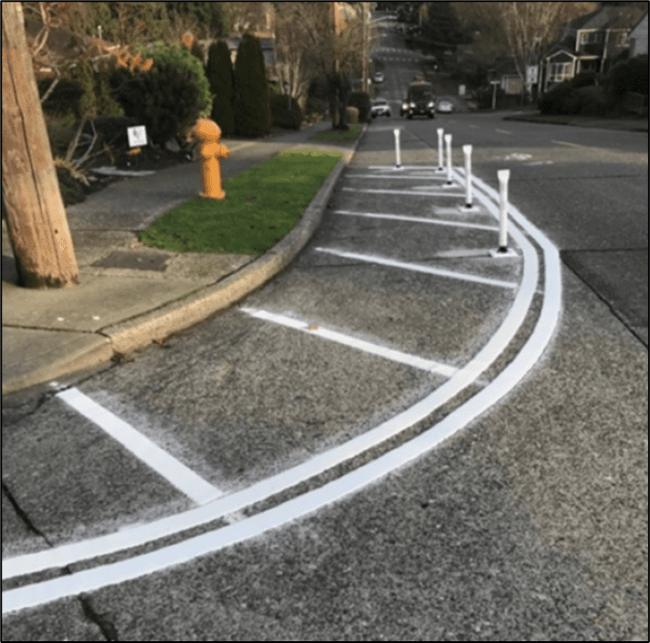 Photo of curb extensions along a sidewalk in West Seattle, which include paint and posts being installed to help improve safety and promote slower travel in residential neighborhoods.