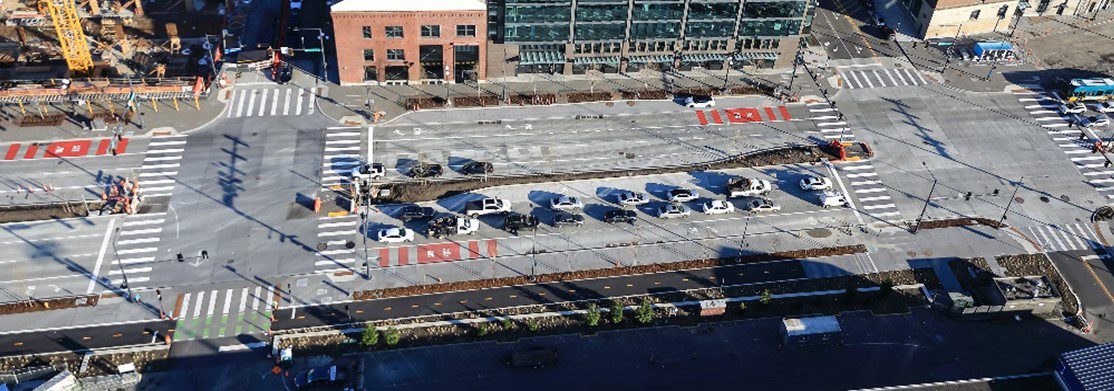 An aerial view of the northbound and southbound transit lanes on Alaskan Way S between S Jackson and S King streets. In the upper the right, south of S King St, a northbound bus can be seen in a transit lane.