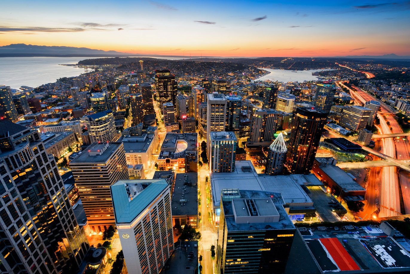 View of downtown Seattle at sunset, looking north. Elliott Bay is visible to the left, Lake Union in the center, and Interstate 5 to the right.