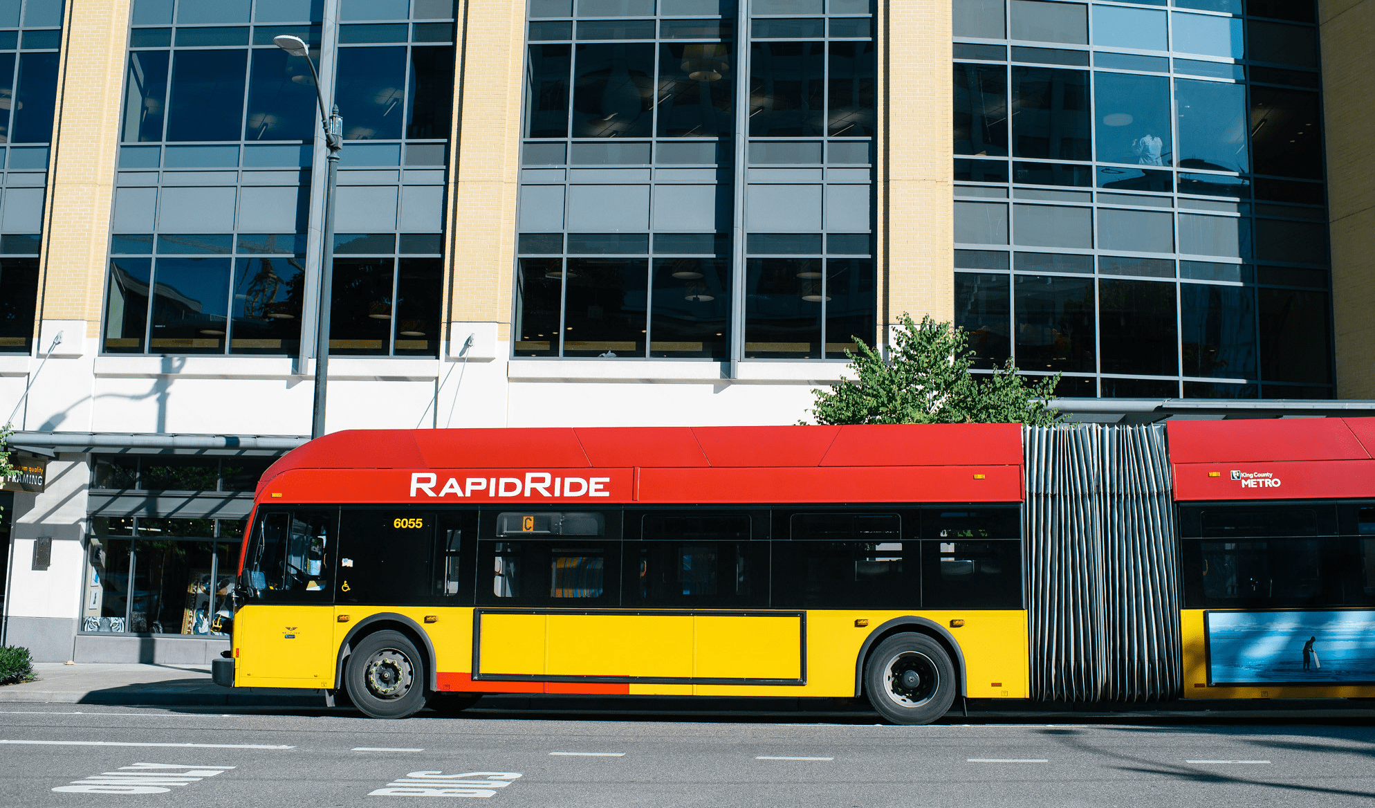 Photo of a RapidRide bus in Seattle. The bus travels on a sunny day, with a large building visible in the background.
