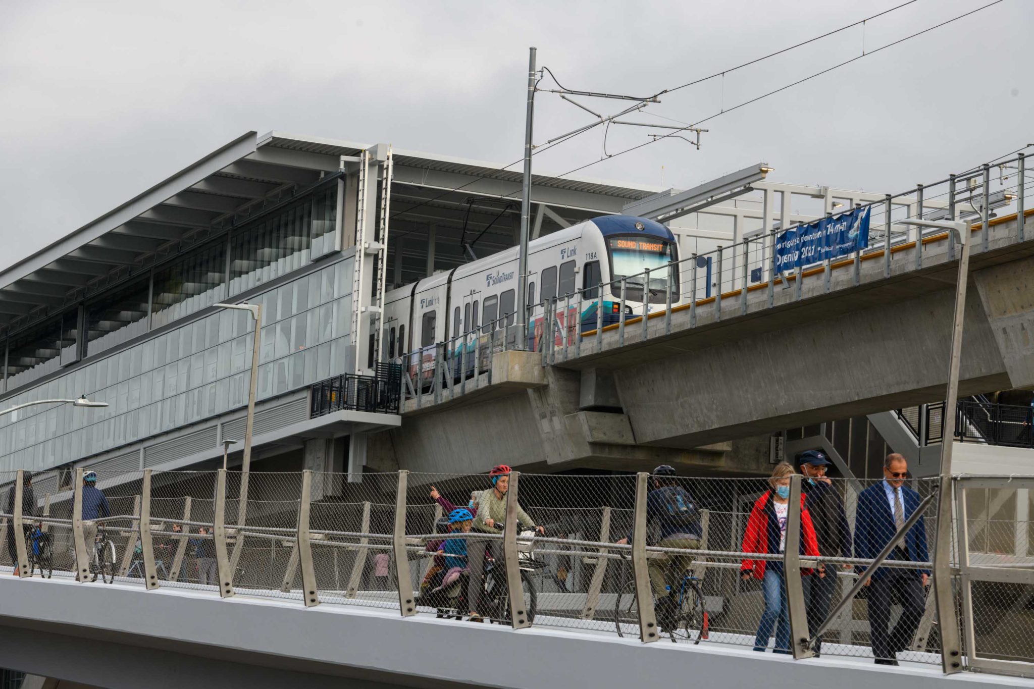People walk and bike on the approach to the new John Lewis Memorial Bridge, as a light rail train departs from the new Northgate station in Seattle. The new bridge for people walking, rolling, and biking, along with the new light rail station, opened in October 2021.