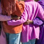 Four women embrace in a hug, in pink, orange, fuchsia, and purple jackets at a photo walk in NYC.