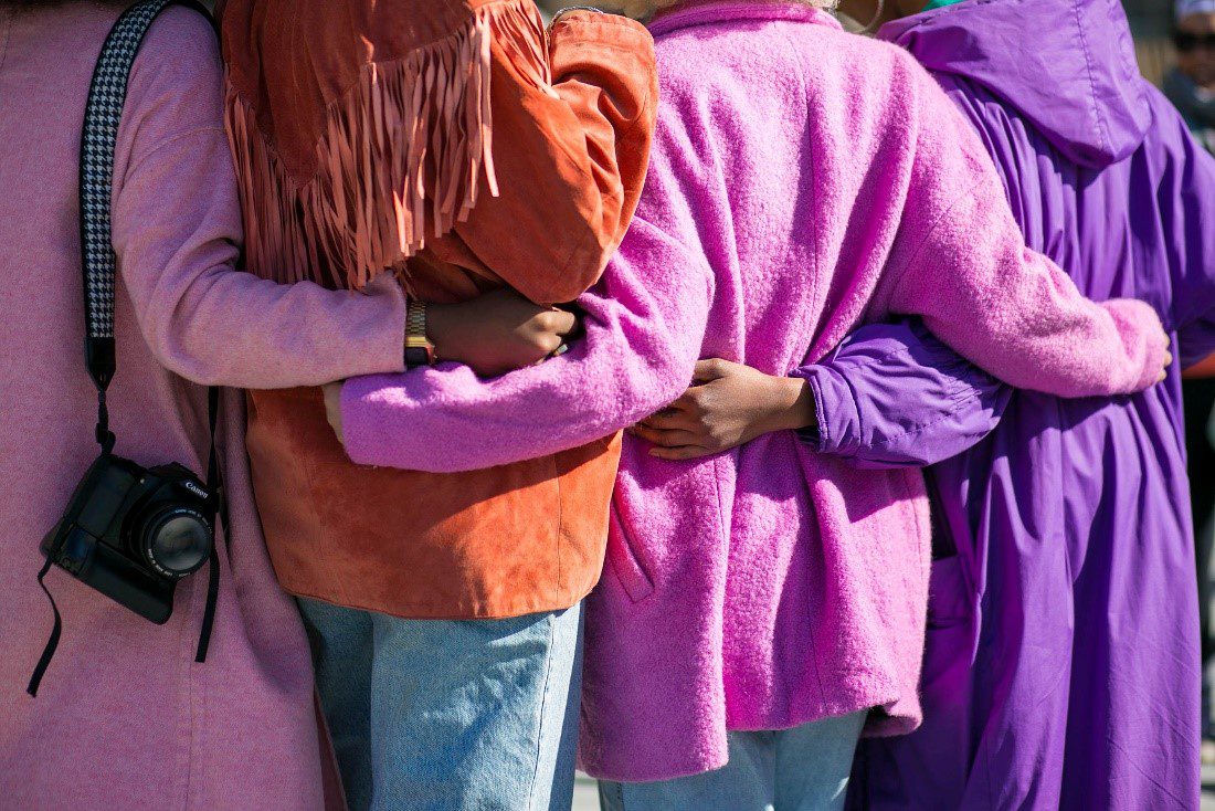 Four women embrace in a hug, in pink, orange, fuchsia, and purple jackets at a photo walk in NYC.