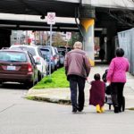 Three people walk across the street and up a curb ramp while pushing a stroller in Seattle.